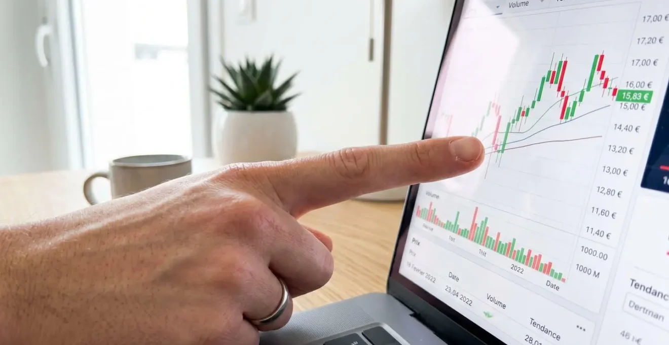 Gros plan sur une main pointant du doigt vers un graphique de prix immobilier affiché sur un écran d'ordinateur portable, l'écran étant volontairement flouté avec un bokeh naturel